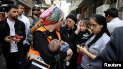 یک مأمور امدادی در حالی که یک کودک متأثر از حملات موشکی جمهوری اسلامی را در آغوش دارد، اشک از صورت کودک دیگر متأثر از این حمله پاک می‌کند