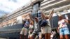 Passengers react after they disembark from the MS Westerdam, back, at the port of Sihanoukville, Cambodia, Friday, Feb. 14, 2020. Hundreds of cruise ship passengers long stranded at sea by virus fears cheered as they finally disembarked Friday and were welcomed to Cambodia. (AP P