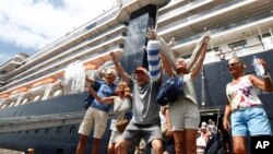 Passengers react after they disembark from the MS Westerdam, back, at the port of Sihanoukville, Cambodia, Friday, Feb. 14, 2020. Hundreds of cruise ship passengers long stranded at sea by virus fears cheered as they finally disembarked Friday and were welcomed to Cambodia. (AP P