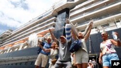 Passengers react after they disembark from the MS Westerdam, back, at the port of Sihanoukville, Cambodia, Friday, Feb. 14, 2020. Hundreds of cruise ship passengers long stranded at sea by virus fears cheered as they finally disembarked Friday and were welcomed to Cambodia.