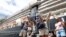 Passengers react after they disembark from the MS Westerdam, back, at the port of Sihanoukville, Cambodia, Friday, Feb. 14, 2020. Hundreds of cruise ship passengers long stranded at sea by virus fears cheered as they finally disembarked Friday and were welcomed to Cambodia.