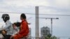 A family travels on a motorbike passing high rises under construction in Preah Sihanouk province, on October 5, 2021. (Sun Narin/VOA Khmer)