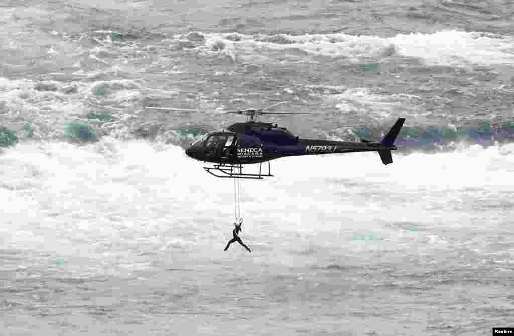 Perempuan seniman akrobatik Erendira Wallenda menggigit tali yang tergantung di helikopter yang terbang di atas air terjun Niagara dalam atraksi di Niagara Falls, New York.