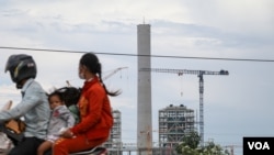 A family travels on a motorbike passing high rises under construction in Preah Sihanouk province, on October 5, 2021. (Sun Narin/VOA Khmer)