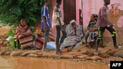 FILE - Sudanese residents sit outside their house at the flooded area of Alqamayir in the capital's twin city of Omdurman, Aug. 26, 2020.