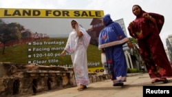 Three women walk past a sign advertising land for sale in Colombo, Sept. 14, 2010.