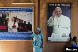 FILE - A woman stands in front of posters of Pope Francis on Nov. 8, 2015, at the Martyrs of Uganda church in Bamako, Mali.