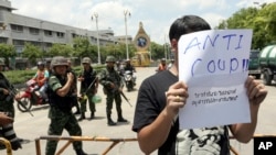 A Thai student holds an anti-coup sign in front of a group of soldiers during a brief protest near the Democracy Monument in Bangkok, Thailand Friday, May 23, 2014. Thailand's ruling military on Friday summoned the entire ousted government and members of 