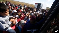 Hungarian police officers stop a group of migrants before boarding a bus that would take the migrants in Roszke, southern Hungary, Tuesday, Sept. 8, 2015. 