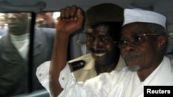 L'ancien président tchadien Hissene Habre (à droite) lève le poing en l'air alors qu'il quitte un tribunal de Dakar escorté par un policier sénégalais, novembre 2005.