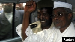 Former Chad President Hissene Habre (R) raises his fist in the air as he leaves a court in Dakar escorted by a Senegalese policeman, November 2005.