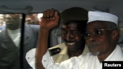 Former Chad President Hissene Habre (R) raises his fist in the air as he leaves a court in Dakar escorted by a Senegalese policeman, November 2005.