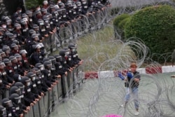 Riot police stand guard as a protester attempts to get through barbed wire barricading the base entrance of the 11th Infantry Regiment, a palace security unit under direct command of the Thai king, Sunday, Nov. 29, 2020, in Bangkok, Thailand.