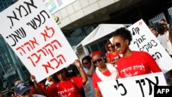 A woman holds a banner reading in Hebrew "don't fear Israel don't fire," left, as Israelis of Ethiopian origin protest in Tel Aviv, July 8, 2019, after a young man of Ethiopian origin was killed by an off-duty police officer in Israel on June 30. 