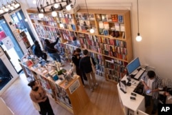 Yu Miao, right, owner of JF Books, looks at his phone as customers browse the books in his bookstore in Washington, Oct. 3, 2024.