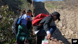 Archivo - Migrantes hondureños cruzan el muro fronterizo hacia EE.UU. en San Diego, California, desde Tijuana, México, el 16 de diciembre de 2018.