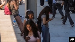 ARCHIVO - Los estudiantes usan sus teléfonos celulares mientras salen de la Escuela Secundaria de Artes Visuales y Escénicas Ramon C. Cortines en el centro de Los Ángeles, el 13 de agosto de 2024. AP