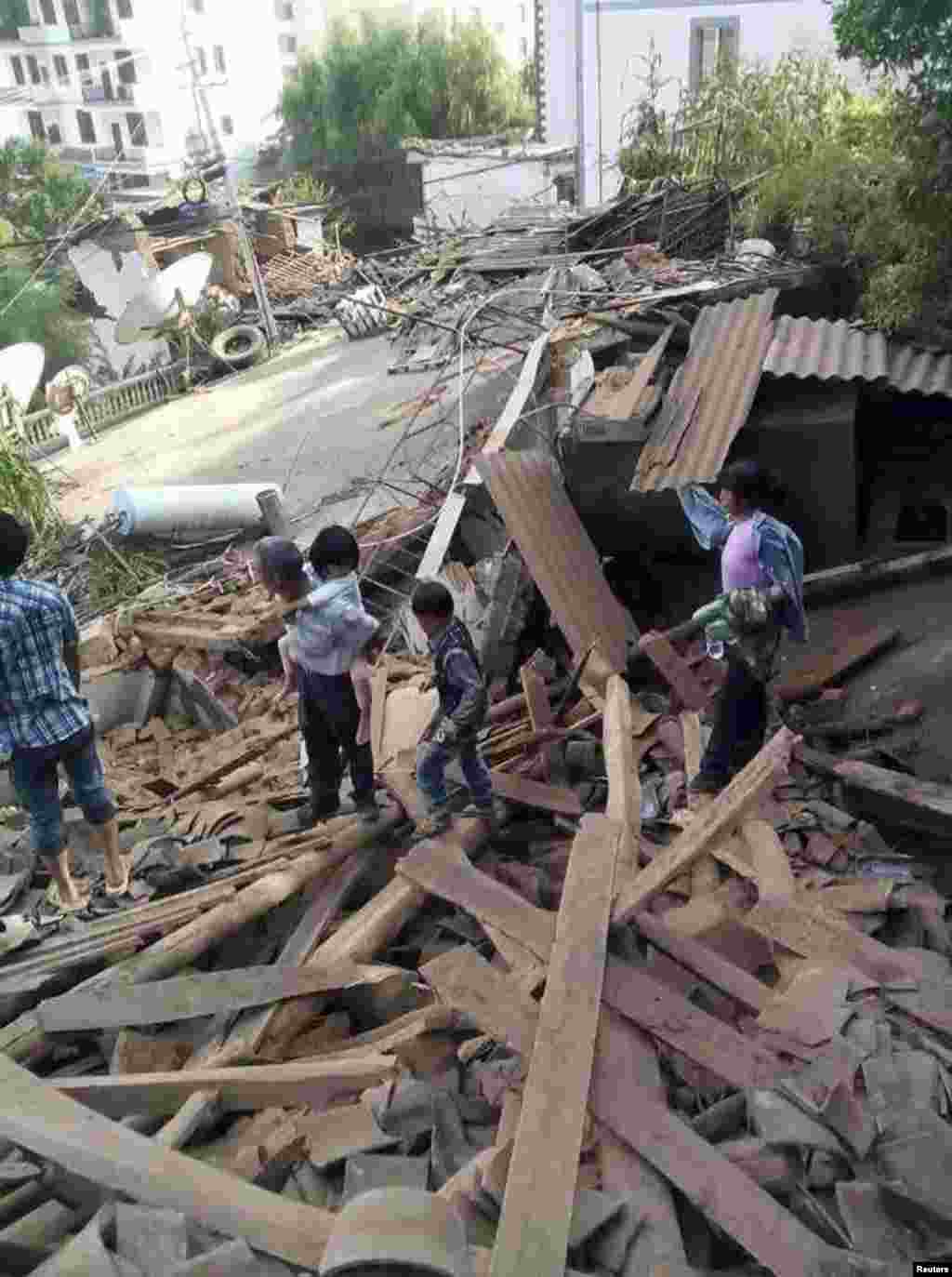 Cư dân đi trên đống đổ nát sau trận&nbsp;động&nbsp;đất mạnh tại huyện Lư Ðiền, tỉnh Vân Nam, Trung Quốc.