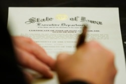 A member of Iowa's Electoral College signs the Certificate of Vote of Electors for the State of Iowa, Monday, Dec. 14, 2020, at the Statehouse in Des Moines, Iowa. (AP Photo/Charlie Neibergall)