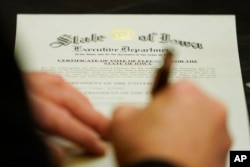 A member of Iowa's Electoral College signs the Certificate of Vote of Electors for the State of Iowa, Monday, Dec. 14, 2020, at the Statehouse in Des Moines, Iowa. (AP Photo/Charlie Neibergall)