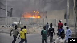 Asap mengepul dari kantor polisi pusat di Kano, Nigeria, sementara warga yang panik berlarian menyelamatkan diri (20/1).