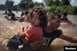 A man, part of a caravan of migrants from Central America en route to the United States, carries a girl through the Suchiate River into Mexico from Guatemala in Ciudad Hidalgo, Mexico, Oct. 29, 2018.