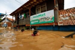 Men swim as they collect items from their houses, flooded after heavy rains in Jakarta, Indonesia, Jan. 2, 2020.