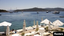 A woman sunbathes on a near-deserted deck as luxury boats are seen anchored off the beach front of a hotel in Golturkbuku, near the resort town of Bodrum on the southwest Aegean coast of Turkey, July 17, 2007. 