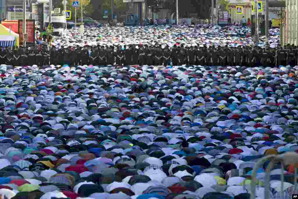 Muslim men, bowing toward Mecca, offer Eid al-Fitr prayers that marks the end of the holy fasting month of Ramadan as police guard them at the main mosque in Moscow, Russia.