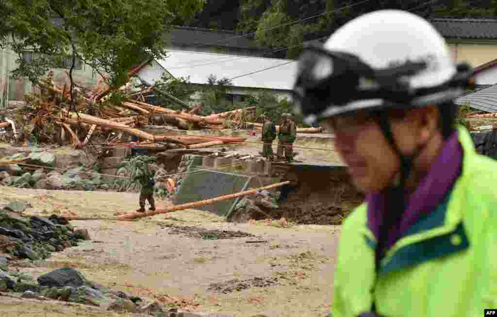 A Japanese Self-Defense Forces officer crosses (L) a river in a disaster area following heavy flooding in Asakura, Fukuoka prefecture. Huge floods engulfing parts of southern Japan are reported to have killed at least six people and left hundreds stranded as the torrents swept away roads and houses and destroyed schools.