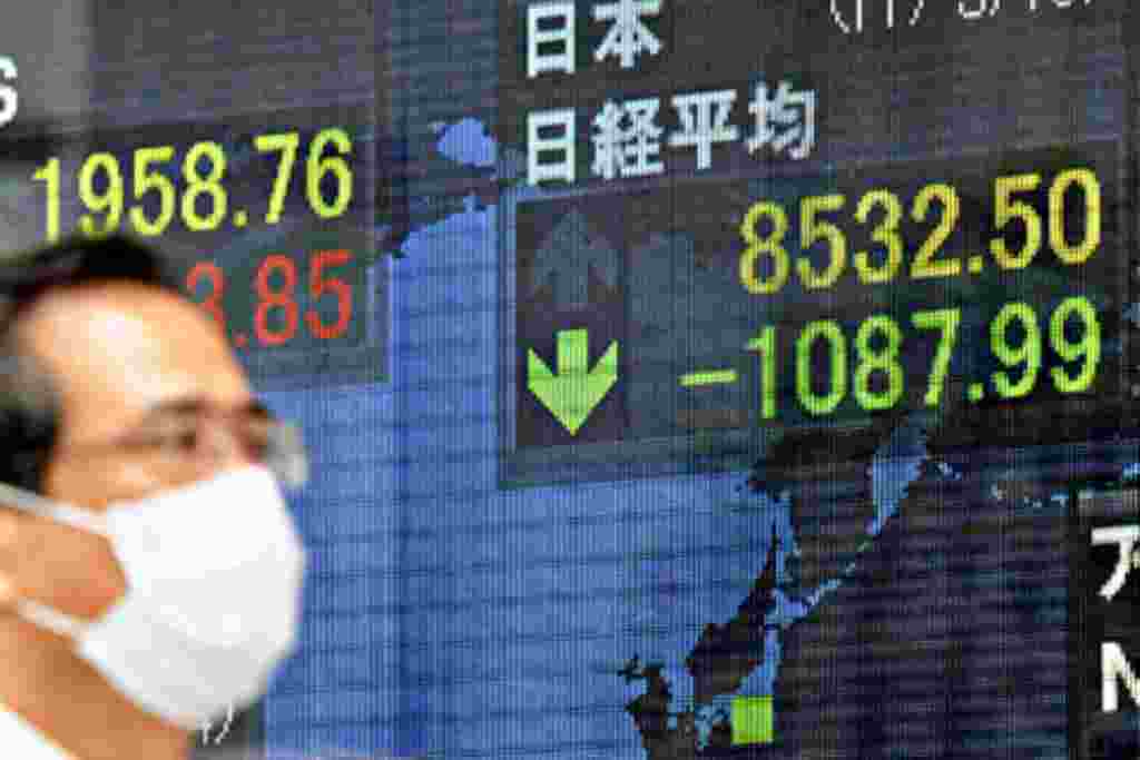 Un hombre camina frente a una pantalla que muestra la caída de precios en los mercados de Tokio.