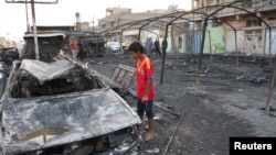 A boy looks at the remains of a burnt-out car at the site of a triple bomb attack in Baghdad's Sadr City, September 22, 2013.