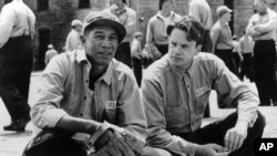 In this photo provided by Courtesy Castle Rock Entertainment via the Library of Congress, inmates Red (Morgan Freeman), left, and Andy (Tim Robbins) share a quiet moment in the prison yard in a scene from "The Shawshank Redemption."