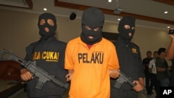 FILE - А suspected drug smuggler, his face obscured with a mask, is escorted by Indonesian Customs officers in Bali, Indonesia, Apr. 27, 2016.