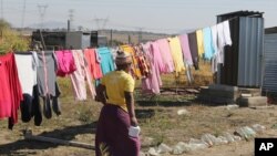 FILE - A woman heads to an outside pit toilet where she shares a shack housing five people, in Marikana, South Africa, Aug. 12, 2016.