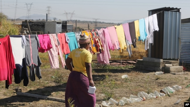 FILE - A woman heads to an outside pit toilet where she shares a shack housing five people, in Marikana, South Africa, Aug. 12, 2016.