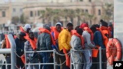 FILE - Caption Migrants disembark after being transferred to Maltese army boats at sea and brought to Valletta harbor, Malta, April 13, 2019.