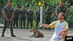 An athlete holds the Olympic Torch by a jaguar during a ceremony in Manaus, northern Brazil, June 20, 2016. The jaguar, who was named Juma and lived in the local zoo, had to be shot dead by soldiers shortly after the ceremony when he escaped. (AFP PHOTO / Diario do Amazonas / Jair Araujo)