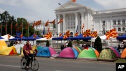 A man on a bicycle passes by tents, posted by the opposition supporters, in front of the government building in Skopje, Macedonia, May 19, 2015. 