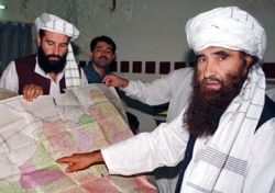 FILE - A 2001 photo of Jalaluddin Haqqani, right, leader of the Haqqani Network, pointing to a map of Afghanistan during a visit to Islamabad, Pakistan while his son Naziruddin, left, looks on.