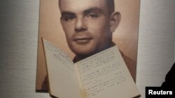 FILE - A notebook belonging to code-breaker Alan Turing is displayed in front of a photo of him during an auction preview in Hong Kong, March 19, 2015. The head of Britain's digital spy agency has apologized for the government's treatment of Turing.