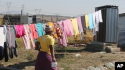 FILE - In this Aug. 12, 2016 photo, a woman heads to an outside pit latrine toilet where she shares a shack housing five people, in Marikana, South Africa. 