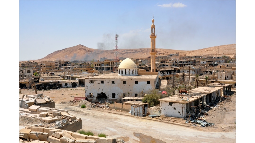 Smoke rises from buildings behind a mosque in the central Syrian town of Al-Sukhnah, situated in the county's large desert area called the Badiya, Aug. 13, 2017.