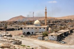 FILE - Smoke rises from buildings behind a mosque in the central Syrian town of al-Sukhnah, situated in the county's large desert area called the Badiya, Aug. 13, 2017.