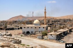 FILE - Smoke rises from buildings behind a mosque in the central Syrian town of al-Sukhnah, situated in the county's large desert area called the Badiya, Aug. 13, 2017.