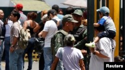 Soldados venezolanos resguardan la entrada de un supermercado en Caracas, mientras la gente hace fila para comprar productos básicos.