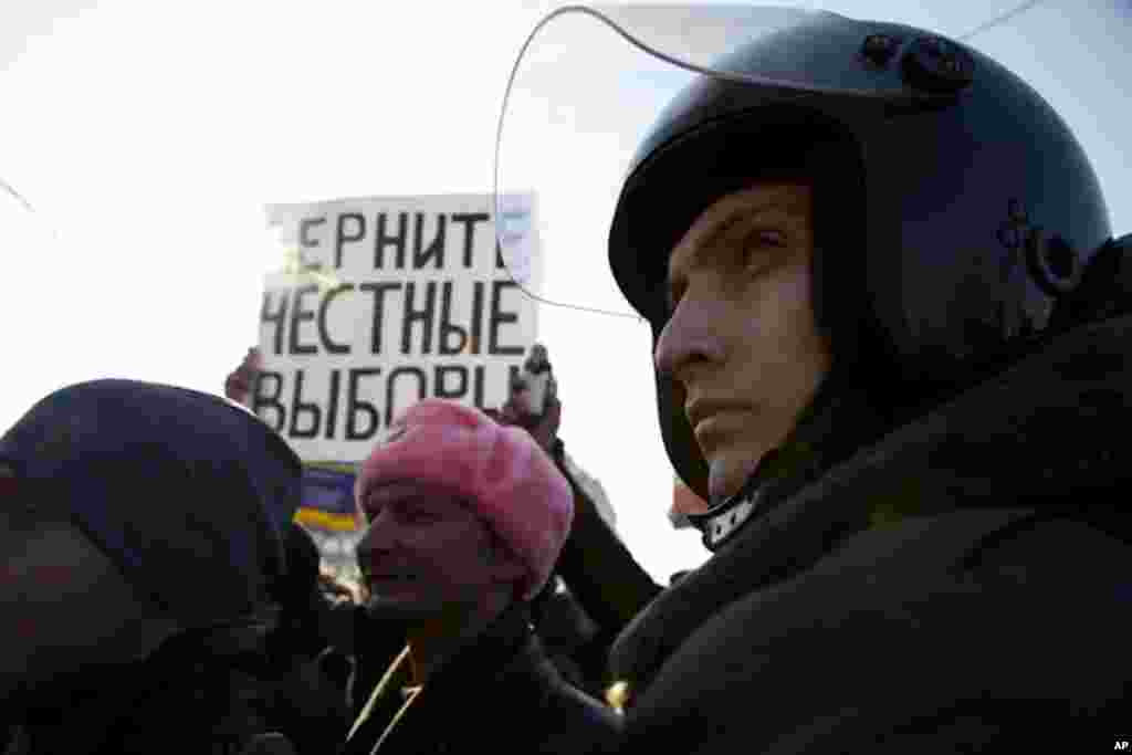 A riot policeman stands in front of a poster that reads, "Give us back fair elections!". (VOA Photo - Yuli Weeks)