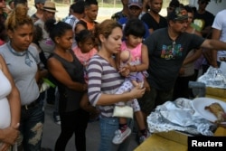 FILE - Asylum-seekers line up for a meal provided by volunteers as they wait in a makeshift migrant camp near the Gateway International Bridge in Matamoros, Tamaulipas, Mexico, June 29, 2019.
