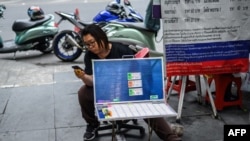 FILE - A vendor selling lottery tickets checks her mobile phone while waiting for customers in Bangkok on March 25, 2019.