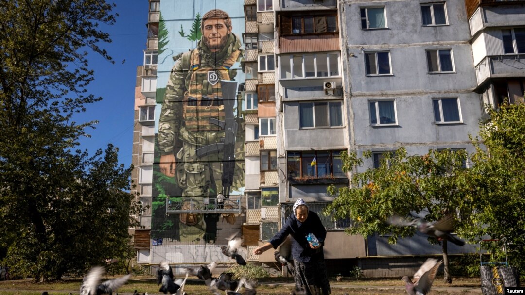 ARCHIVO - Una mujer alimenta palomas frente a un mural del artista callejero ucraniano Eugene Gladenko que muestra al soldado ucraniano caído Maksym Bordus, en medio del ataque de Rusia a Ucrania, en Kiev, Ucrania, el 8 de octubre de 2024.